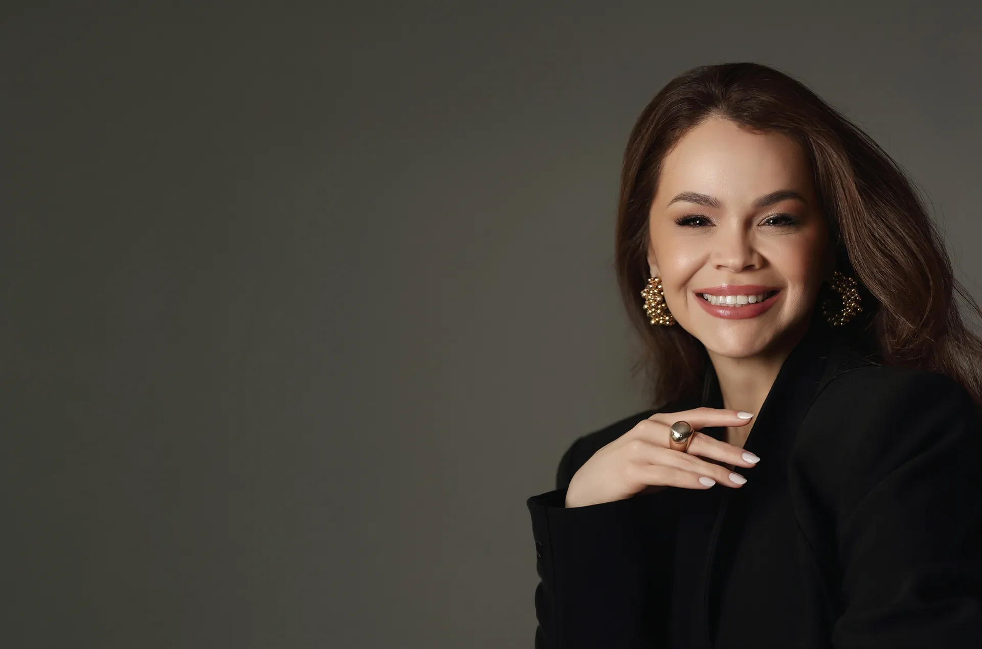 Dra. Vanessa Soares, dermatologista em Curitiba, sorrindo, de blazer preto e brincos dourados.